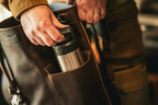 Close-up of man pulling tumbler from Zunera leather backpack side pocket